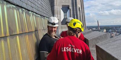 Lesgevers en monumentenwachter op hoogte aan buitenkant belfort